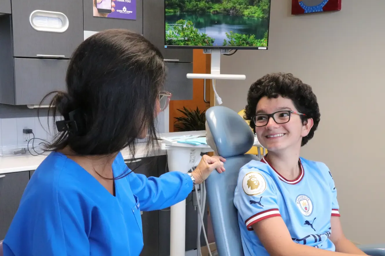 A team member in blue scrubs talking with a smiling young patient in the dental chair